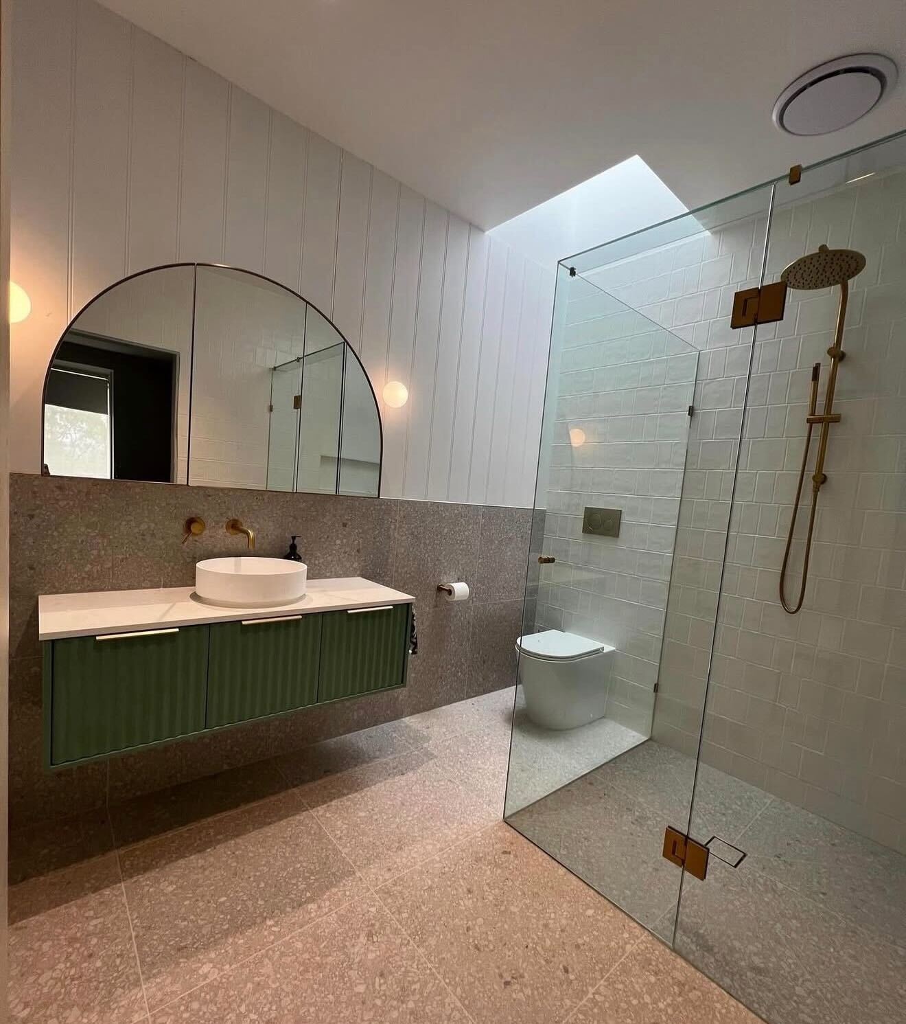 Bathroom with green ribbed vanity, arched mirror and glass shower